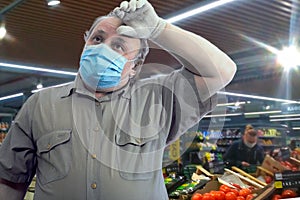 A man in a short-sleeve shirt, medical mask and gloves wearily wipes the sweat from his forehead with his hand