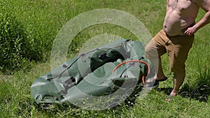 A man in shorts, inflate rafting boat with pump.