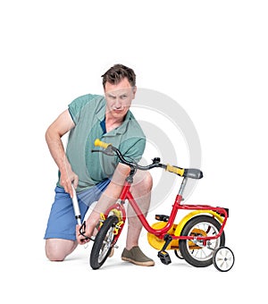 Man in shorts and a t-shirt pumping wheel at children`s bike. Isolated on white background.
