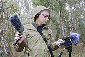 The man with Shotgun Condenser Microphone and headphones is recording the sounds of nature.