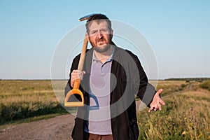 A man with a shovel in the field is provocatively behaving