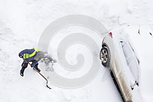 Man shoveling snow near car on parking. Top view