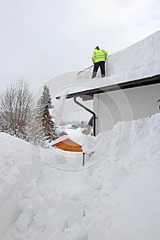 A man shovels dangerously heavy snow from a house roof