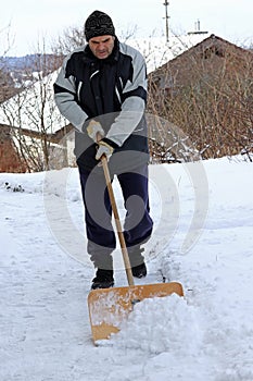 A man shovels snow from a sidewalk in the winter