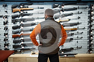 Man at showcase with rifles, back view, gun shop