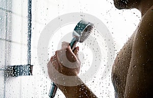 Man in shower. Water splash drops on bath cabin stall glass. Faucet head in hand. Public gym, hotel or home bathroom.