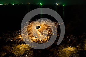 Man showers of glowing sparks from spinning steel wool on rocky