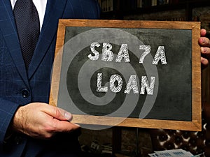 Man showing black chalkboard with written text Small Business Administration SBA 7A LOAN . Blurred background. Horizontal mockup