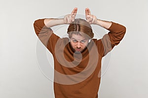 Man showing bull horn gesture with fingers over head, looking hostile and threatening.