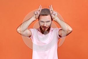 Man showing bull horn gesture with fingers over head, looking hostile and threatening.