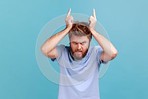 Man showing bull horn gesture with fingers over head looking hostile and threatening aggressive face