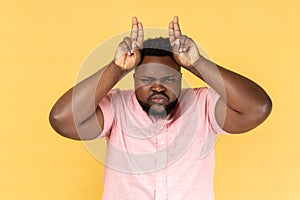 Man showing bull horn gesture, looking at camera with hostile angry expression threatening to attack