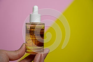 Man showing cosmetic serum bottle on pink and yellow background,Protector skin Treatment facial essence oil, Vitamin C. Beauty and photo