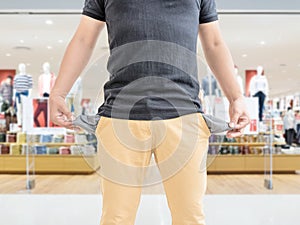 Man showing his empty pockets on blur shopping mall