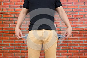 Man showing his empty pockets on brick wall