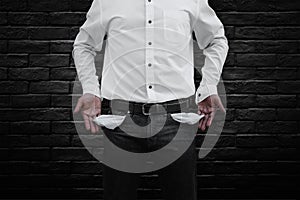 Man showing his empty pockets on dark brick wall background