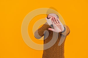 Man showing his open palm and covering his face ashamed - stop gesture - orange background