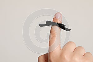 Man showing index finger with black tied bow as reminder on white background, closeup. Space for text