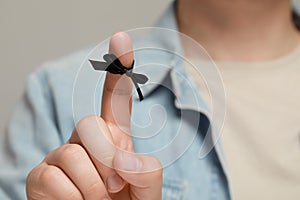 Man showing index finger with tied bow as reminder against light grey background, focus on hand