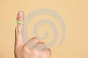 Man showing index finger with tied bow as reminder on beige background, closeup. Space for text