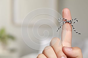 Man showing index finger with tied bow as reminder on blurred background, closeup. Space for text