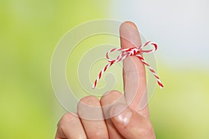 Man showing index finger with tied bow as reminder on green blurred background, closeup