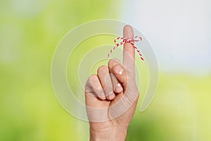 Man showing index finger with tied bow as reminder on green blurred background, closeup