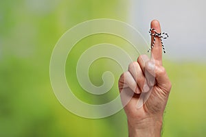 Man showing index finger with tied bow as reminder on green blurred background, closeup. Space for text