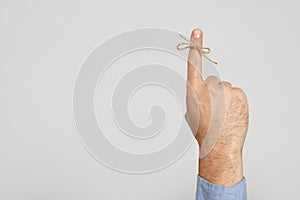 Man showing index finger with tied bow as reminder on light grey background, closeup. Space for text