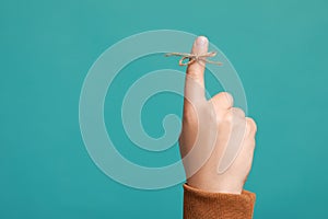 Man showing index finger with tied bow as reminder on turquoise background, closeup. Space for text