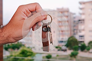 Man showing keys to a new house in front of blurred condos, the image of the house key used for real estate ads