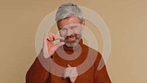 Man showing a little bit gesture with sceptic smile, showing minimum sign, measuring small size