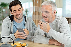 man showing mature father something on smartphone