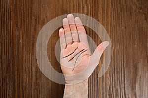 Man showing palm with drawn lines on wooden background. Chiromancy and foretelling photo
