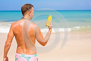 Man showing sun protection cream bottle on the beach