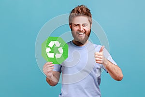 Man showing thumbs up, holding green waste recycling symbol, satisfied with environmental safety.