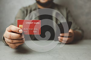 Man shows a red credit card and holding his phone. Shopping online by credit card with online service