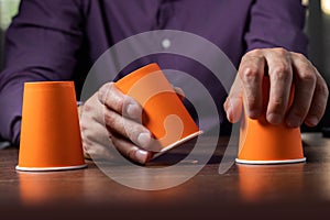 Man shows shell game of thimbles with coin, dark background. Concept deception, sleight hand