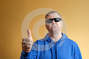 A man shows a thumbs up gesture. Portrait of a man in a blue hoodie and sunglasses