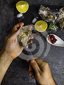 A man shucking fresh oysters with his bare hands on stone table, lemon slices, micro greens, ice, cranberries on table