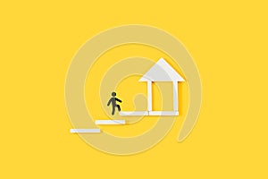 Man sign climbing wooden steps with a house made with wooden blocks at the top on a yellow background