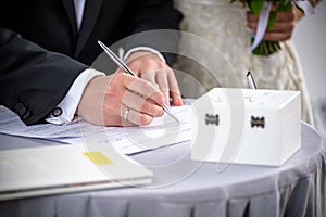 Man signing a marriage register as a groom or witness with a stylish fountain pen with two wedding rings and red flowers, symbolic