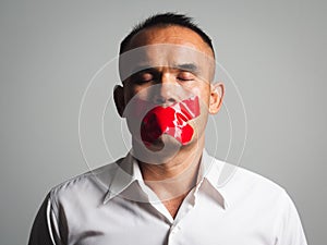 Man is silenced with adhesive red tape across his mouth sealed to prevent him from speaking. Freedom Concept