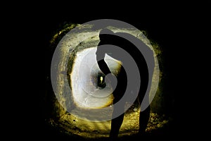 Man silhouette in a cave or dry sandstone water channel, back shot. Visiting of old underground