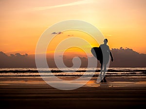 Man silhouette holding surfing board, walking on dark seashore with copy space. Surfer standing on sunset sky over the sea water