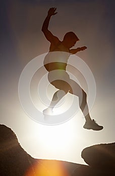 Man, silhouette and jump on rock at sunset with freedom, adventure and challenge on mountain or cliff. Climbing, hill