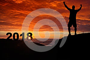 Man silhouette on the mountain top watching the sunrise and 2018 years while celebrating