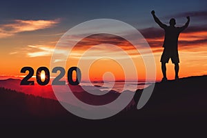 Man silhouette on the mountain top watching the sunrise and 2020 years while celebrating