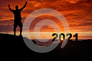 Man silhouette on the mountain top watching the sunrise and 2021 years while celebrating