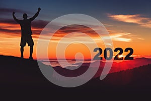 Man silhouette on the mountain top watching the sunrise and 2022 years while celebrating